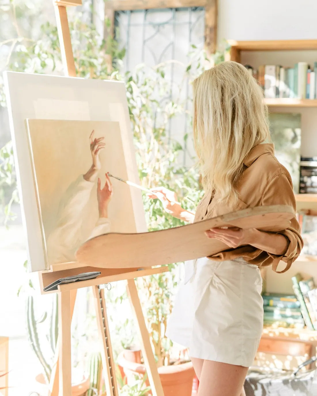 An artist painting a canvas on an easel in a sunlit studio